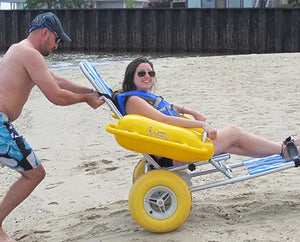 Man pushing a woman through the sand in an Accessrec  WaterWheels Floating Beach Wheelchair