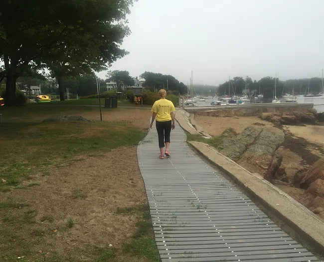 A Woman Walking Down a AccessRec Mr Boardwalk Beach Access Mat 