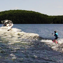 Load image into Gallery viewer, Rave Impact™ Red Brick wakeboard with Youth bindings with a boat pulling the boy.
