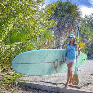 A woman walking carying Pulse The Seafoam 10'6" Tradisional SUP