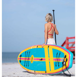 A woman holding the POP Board Co 11'0 Yacht Hopper Turq/Pink/Ylw Stand Up Paddle Board